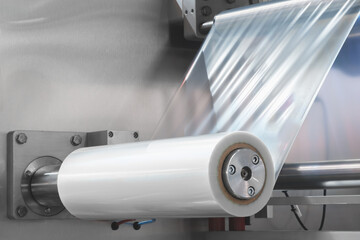 A machine with a roll of polyethylene plastic film on it. The machine is in a factory. industrial...
