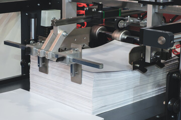 Stack of papers is on a conveyor belt. papers are white and are stacked on top of each other, packaging concept background