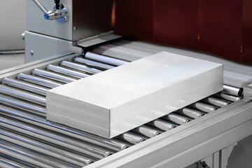 White cardboard box in protective polyethylene film stands on conveyor belt. Packaging delivery...