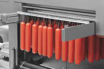 conveyor belt with red meat sausages hanging on it. The hot dogs are lined up and all the same...