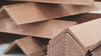 Stack of cardboard corner protectors for packaging, corners are brown and arranged in a row as...