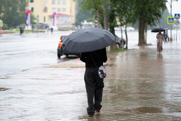 It's raining in the city. A man with an umbrella is walking through the city.