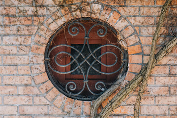 Round Brick Wall Window with Ornamental Wrought Iron Grille and Climbing Vine