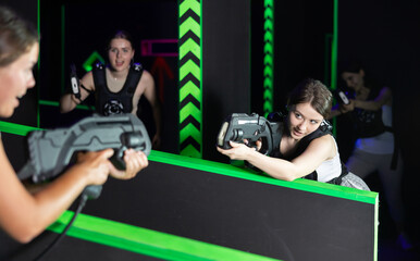 Portrait of excited girlfriends playing enthusiastically laser tag game two teams opposite each...
