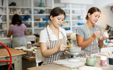 Young woman teacher and young girl student sculpt and paint ceramics in workshop