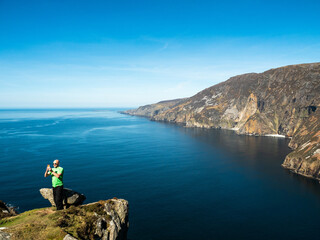 Male tourist is sightseeing stunning Slieve League cliff nature scenery and Atlantic ocean. Blue...