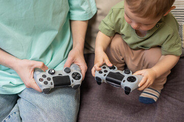 Caucasian woman teaches her little son to play console. Joystick in hands. 