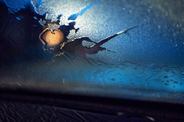 Car front glass covered with frosted ice and defrosted patch with blue sunrise sky. Cold winter...