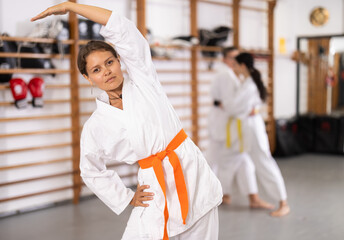 Sportive young girl wearing kimono doing exercises in large sports hall