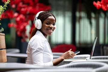 Portrait of happy female black freelancer working on laptop computer outdoors.