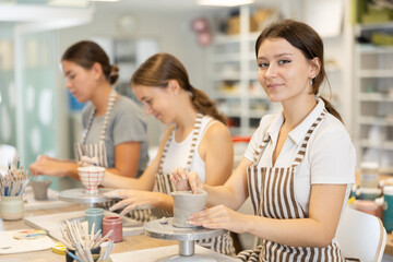 Young woman teacher and two girls students sculpt from clay and paint pottery