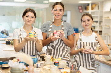 Three girls visitor to course on creating ceramic products shows off final product, shows painted...