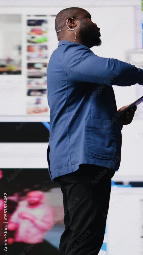 Poster vertical video black presenter hosting conference on stage surrounded by media visuals, symbolizing 
