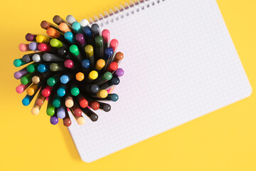 Back to school banner. Multicolored pencils on a stand and a notebook on a yellow background. Ideal for school themes and educational projects