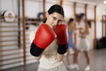Young woman in sportswear and boxing gloves stands in the gym against the background of people...