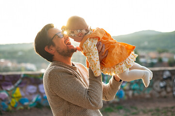 Father lifting his baby daughter at sunset, laughing outdoors