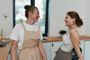 Obraz premium Middle age woman smiling and interacting with a younger woman, promoting active, healthy lifestyle, wellbeing, and wellness in a cozy modern home kitchen.