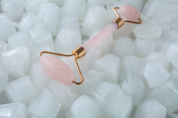 Pink face roller scraping for aesthetic facial massage on ice cubes and water background. Selfcare...