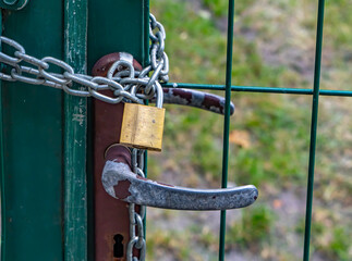 Close-up of an old metal gate locked with a chain and brass padlock. Concept of security, privacy,...