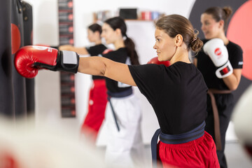 Sportive young female practitioner of boxing courses training with punching bag during workout...