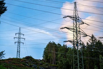 Steel power pylons with wires stretching across a rocky forest hillside. Captured at dusk with...