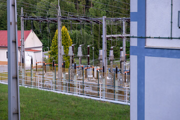 Modern electric substation with high-voltage equipment, surrounded by greenery and buildings. Part...