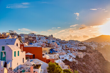 Fototapeta premium Aerial drone view of famous Oia village with white houses and blue dome churches during sunrise on Santorini island, Aegean sea, Greece.