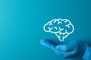 Mental health awareness concept. Doctor's hand in a blue glove gently holding a brain icon, symbolizing care,support,mental wellness, psychology,depression,anxiety.Blue background with copy space.