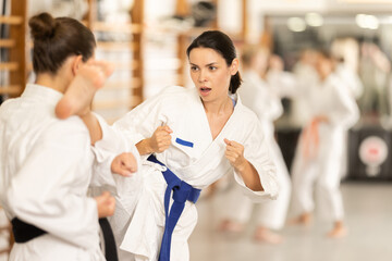 Sportive young woman in kimono applying attack methods on girl during karate courses