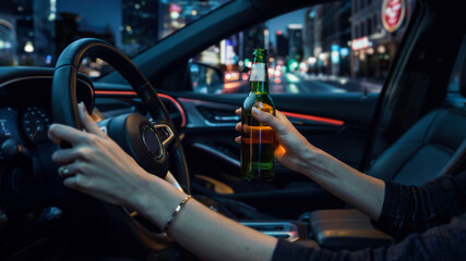 Obraz premium Interior of a car at night. Female driver with one hand on the wheel and the other holding a beer bottle. Blurred city lights outside.