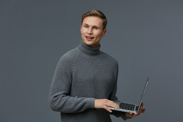 smiling man in gray turtleneck sweater standing hold laptop use digital nomad concept on gray...