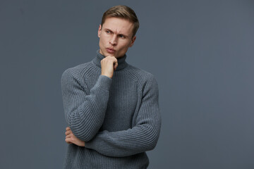 Thoughtful young man with light skin and short hair, wearing a cozy gray turtleneck sweater, looks...