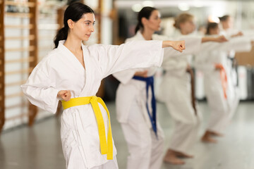 Sportive female practitioner of karate courses performing punches in sports hall