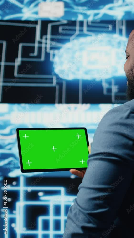 Poster vertical video black it specialist examining algorithmic data next to chroma key, using tablet in a 