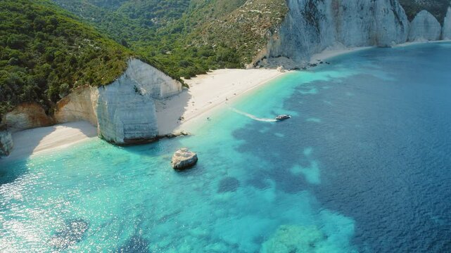 Speedboat passing near white cliffs and sandy beach with turquoise sea in Kefalonia Greece