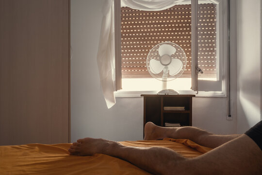 Man trying to sleep during a heat wave using an electric fan