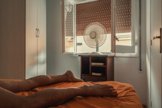 Man trying to sleep during a heat wave using a fan.