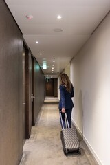 A determined businesswoman in an elegant suit confidently walks down a hotel corridor, rolling her...