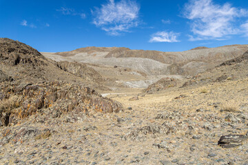 Expansive arid landscape featuring rocky terrain and distant hills under a bright blue sky with scattered clouds, showcasing the beauty of nature's rugged environment