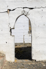 Cracked white wall with an arched doorway reveals a glimpse of the outside landscape, showcasing...