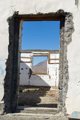 Abandoned building with weathered walls and door frames, showcasing a view through openings towards a clear blue sky and distant mountains, evoking a sense of nostalgia and decay
