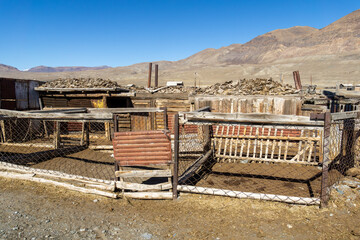 Abandoned wooden structures with rustic fences and rocky terrain under clear blue sky, showcasing...