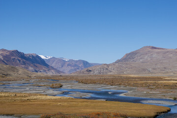 Scenic landscape featuring a winding river flowing through a vast valley surrounded by majestic mountains under a clear blue sky showcasing natural beauty and tranquility
