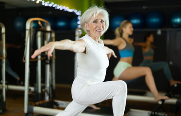 Mature woman on a group Pilates training performs leg exercises on a reformer. Client of a fitness...