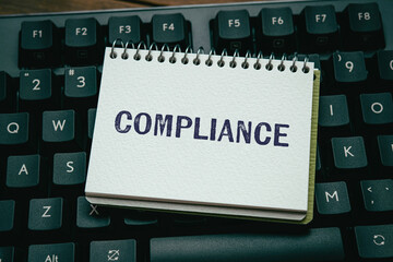 There is notebook with the word Compliance. It is as an eye-catching image.