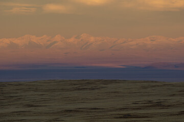 Majestic mountain range with snow-capped peaks under a colorful sky at sunset, casting reflections...