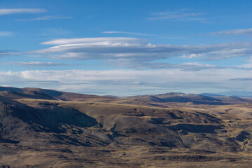 Expansive view of rugged terrain under a vast blue sky with scattered clouds, showcasing the natural beauty and geological features of the landscape in a serene environment
