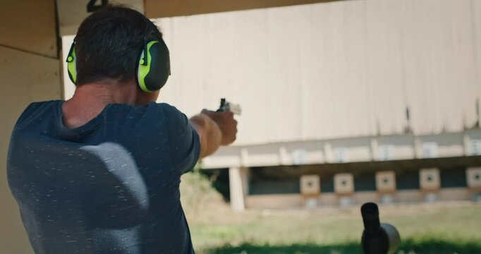 Man firing revolver at an outdoor shooting range with earmuffs