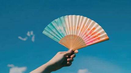 Hand holding a colorful paper fan against a vibrant blue sky