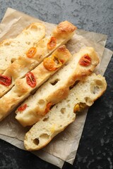 Pieces of delicious focaccia with tomatoes on dark textured table, top view